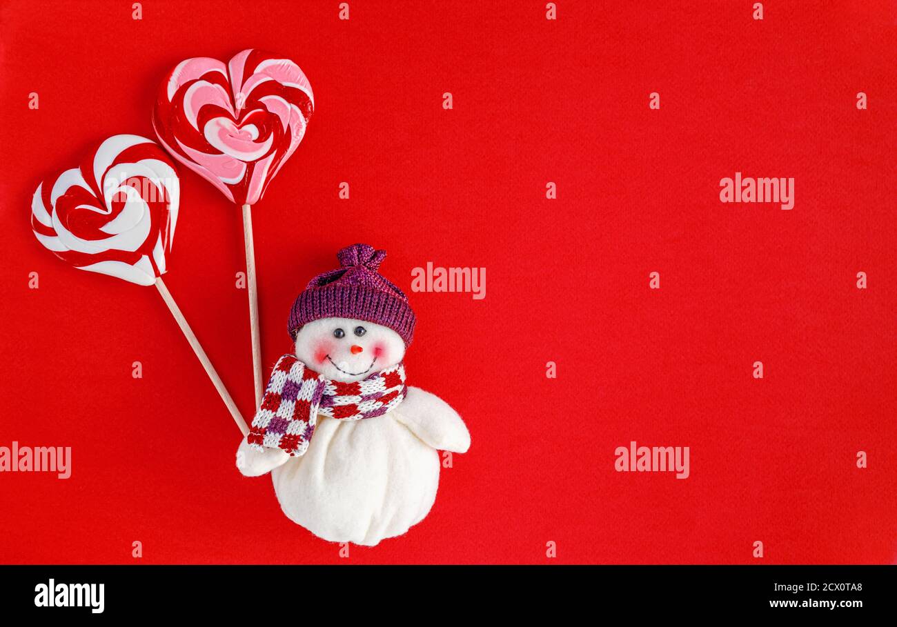 Schneemann hält traditionelle Weihnachtsgeschenke in Herzform auf rotem Hintergrund. Grußkartenkonzept Stockfoto