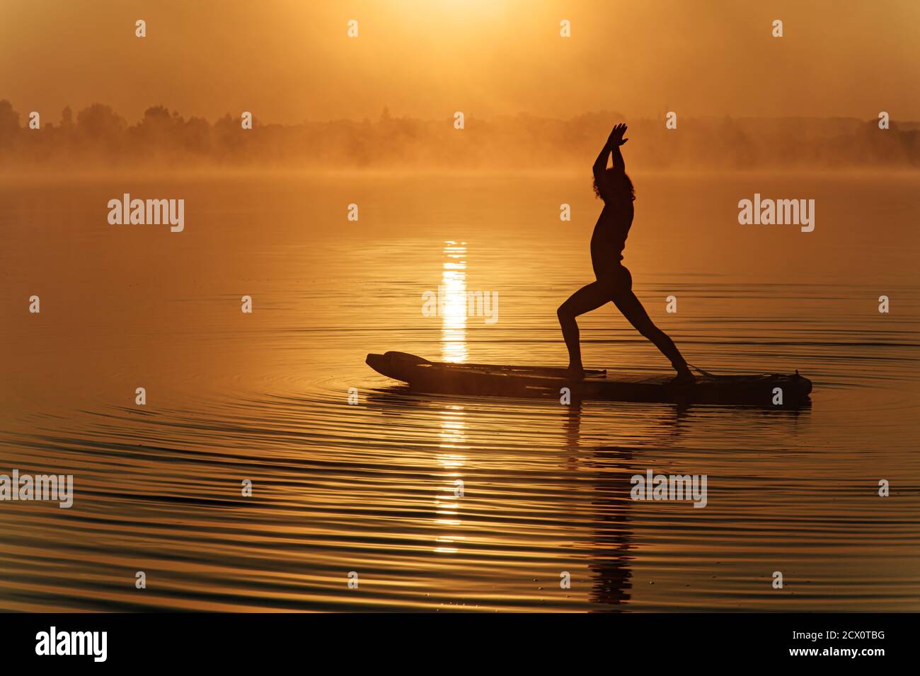 Silhouette eines sportlichen Mannes, der Yoga auf dem Paddle Board macht Stockfoto