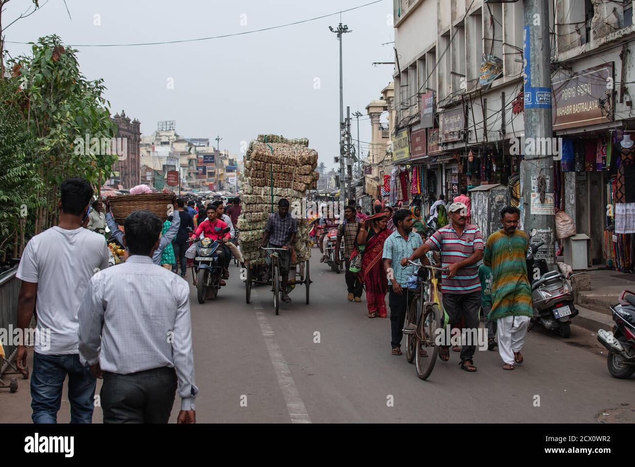 Puri, Indien - 3. Februar 2020: Nicht identifizierte Menschen gehen auf einer Straße, als ein nicht identifizierter Mann am 3. Februar 2020 schwere Ladung auf einer Rikscha transportiert Stockfoto