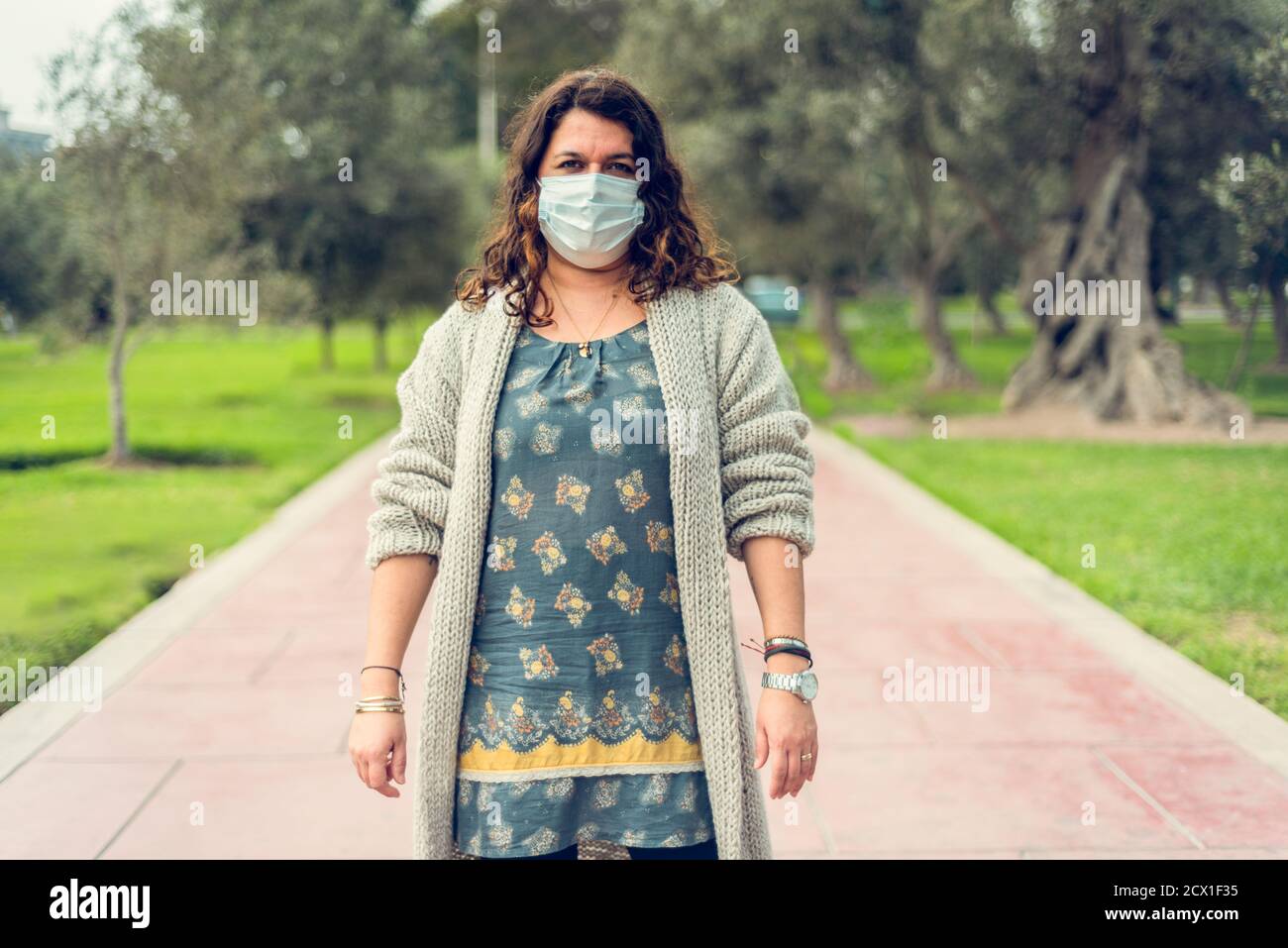 Junge Frau bedeckt sich mit einer Schutzmaske auf dem Feld, um ein Virus zu vermeiden. Coronavirus-Konzept. Stockfoto