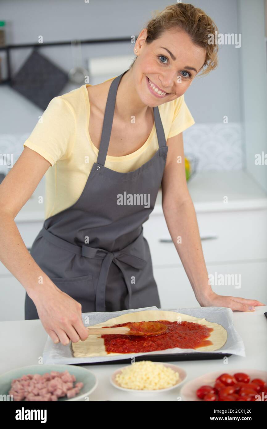 Frau, die Tomatensauce auf Pizzabasis zugab Stockfoto