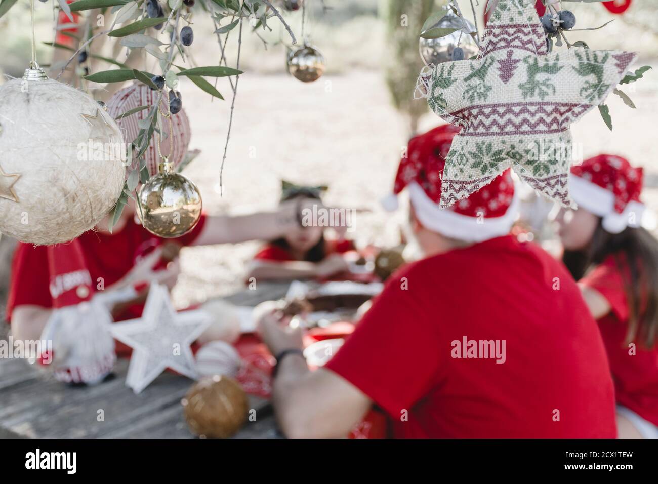 Eine Familie, die durch Unschärfe nicht identifiziert wurde und ein weihnachtliches Picknick im Freien in roten und Weihnachtsmützen mit Weihnachtsdekorationen an einem Tre feiert Stockfoto