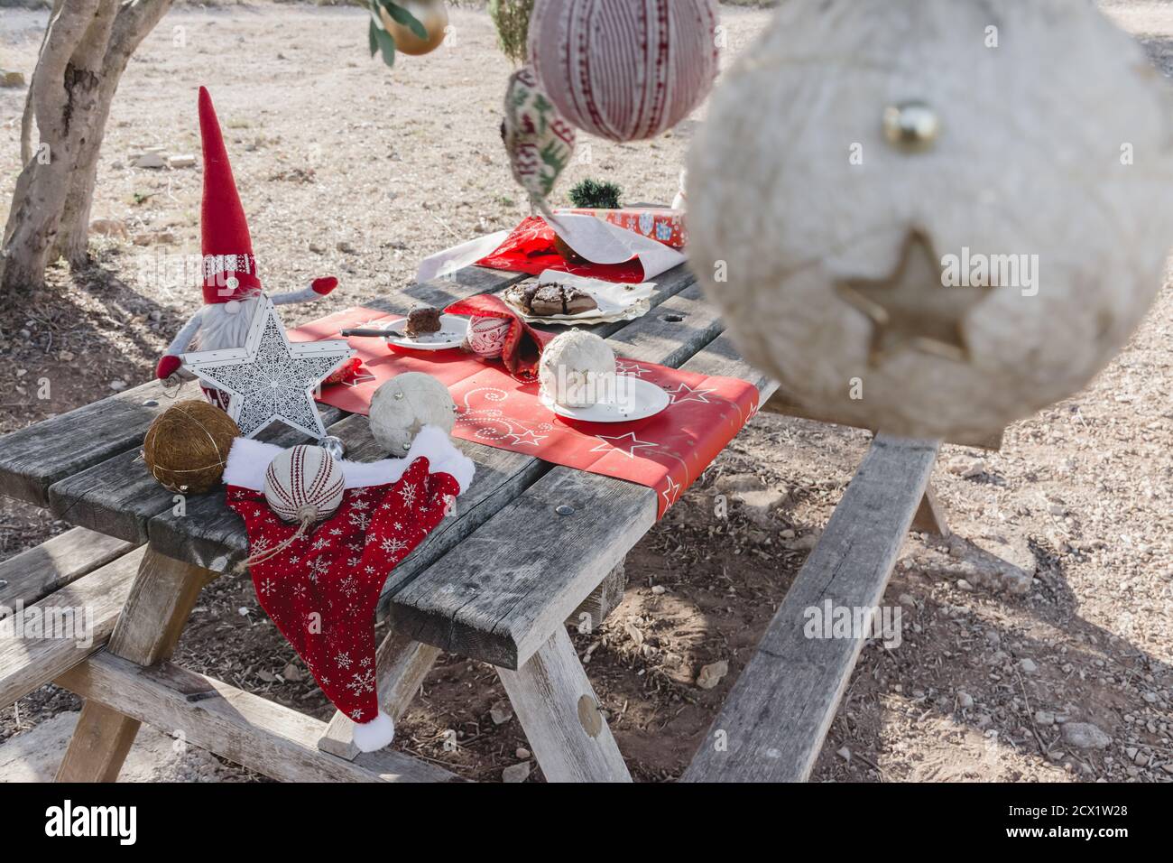 Picknicktisch mit weihnachtsschmuck auf dem Feld mit Überresten Von einem weihnachtskuchen und Dekorationen hängen von den Zweigen Eines Baumes Stockfoto