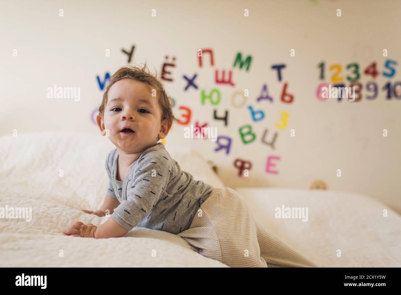 Baby kriecht auf weißem Bettüberwurf mit Buchstaben und Zahlen Wand Stockfoto