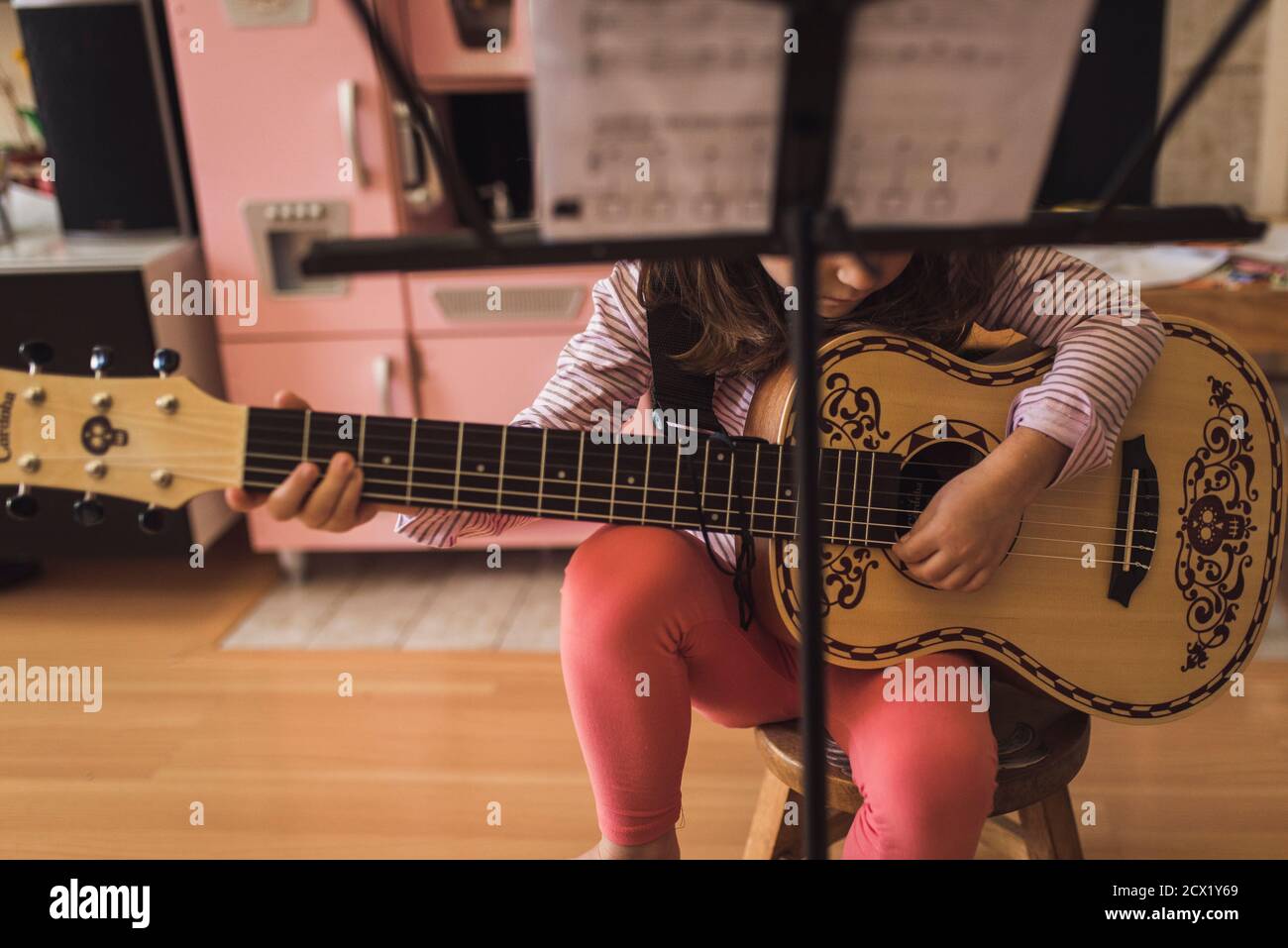 Junges Mädchen auf Hocker sitzen Kommissionierung die Fäden von klein Verzierte Gitarre Stockfoto