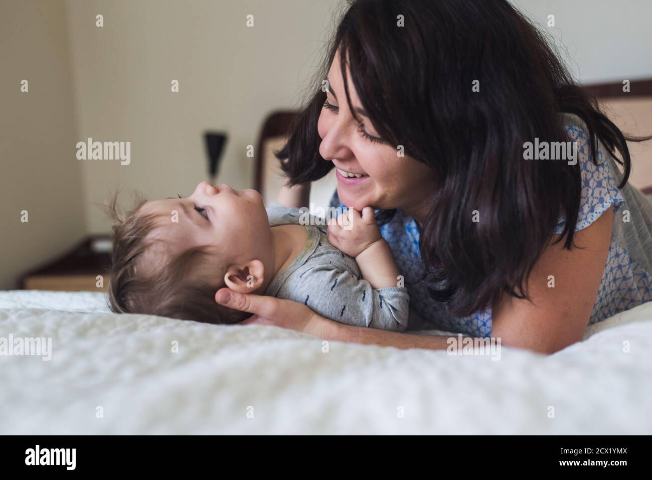 Lächelnde Mitte der 30er Jahre Mutter mit dunklen Haaren liebevoll bewundernd Baby auf Bett Stockfoto