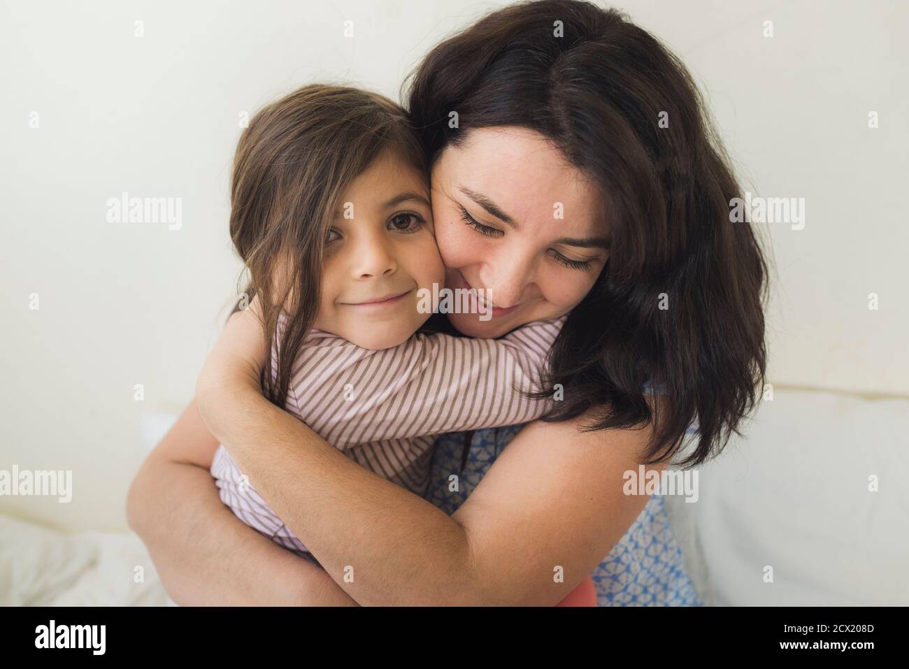 Lächelnde Mutter Mitte der 30er Jahre umarmt glückliche 6-jährige Tochter Stockfoto