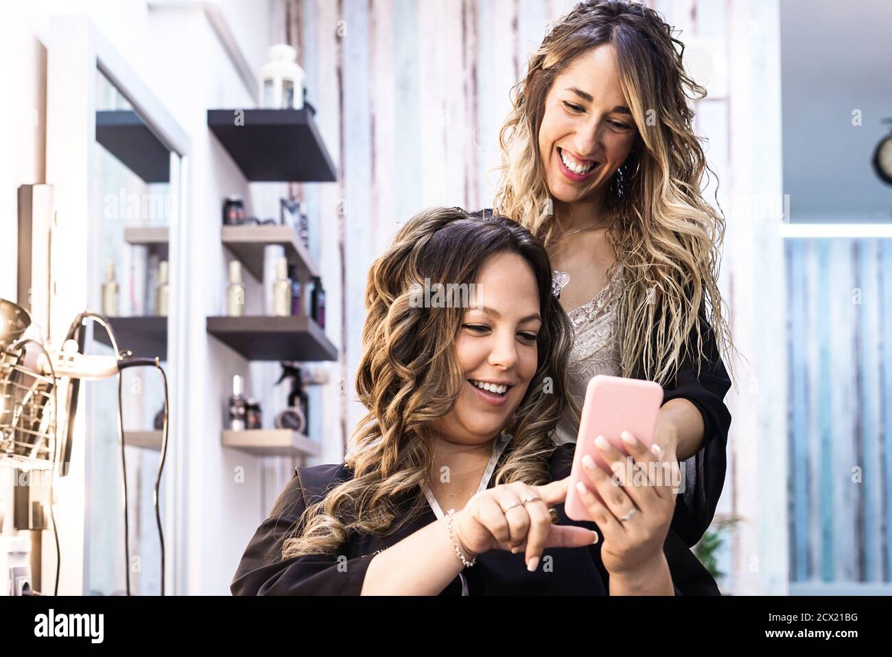 Frau mit Smartphone und Friseur macht Haar Styling im Salon Stockfoto