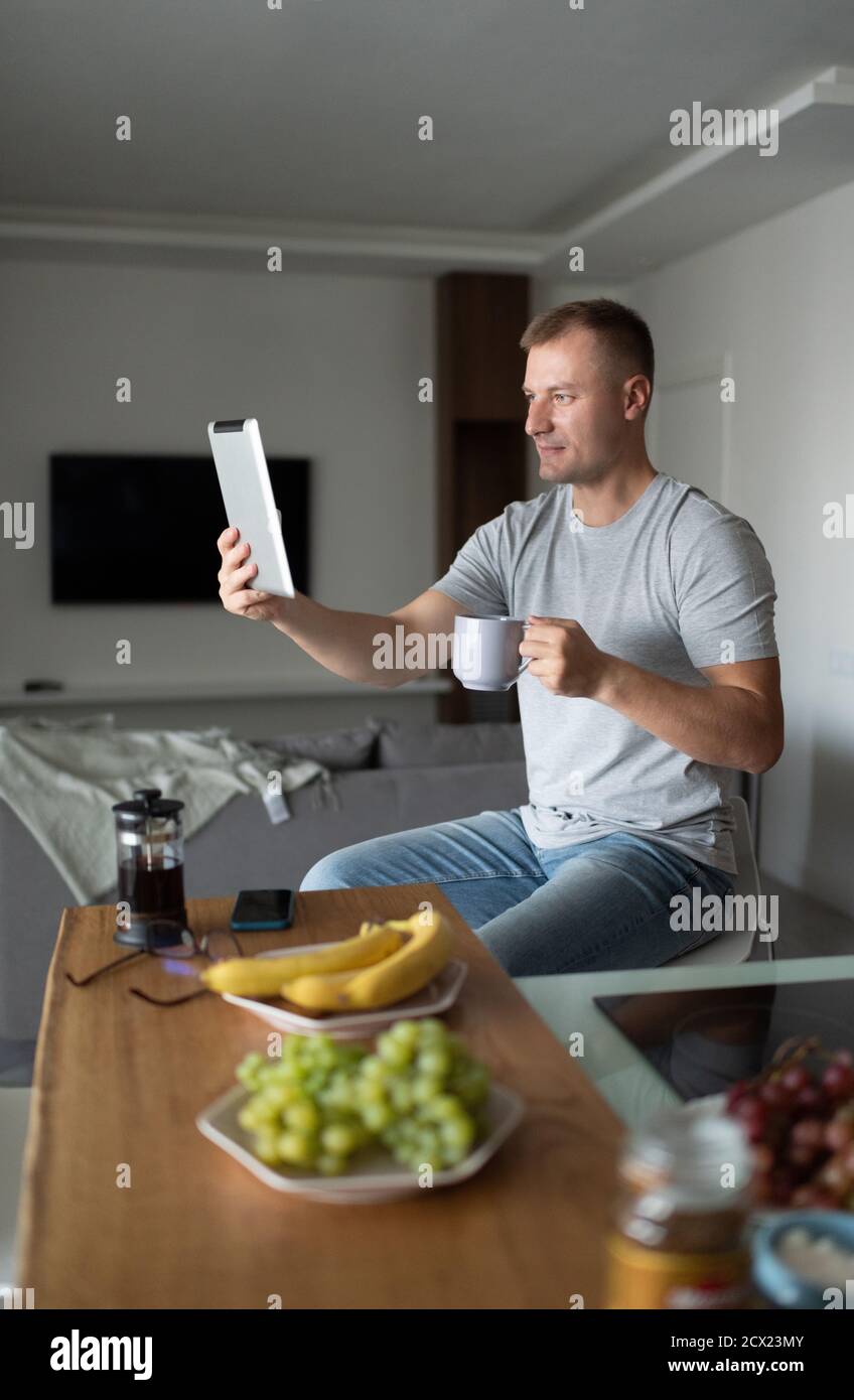 Erwachsene männlich trinken heißes Getränk und machen Video-Anruf zu Freund am Morgen Stockfoto