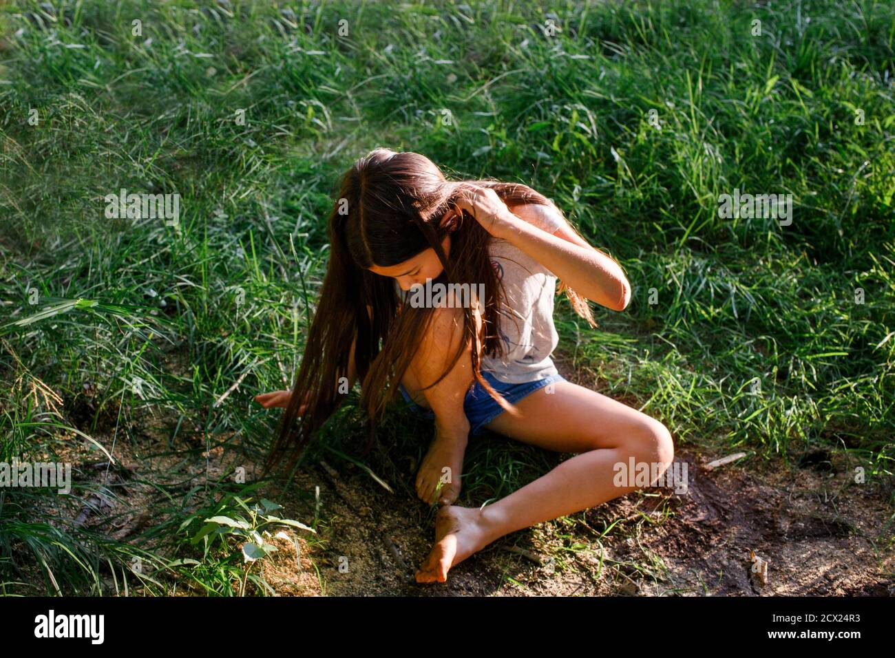 Oben-Ansicht des jungen Mädchens, das im Gras mit schlammigen Füßen sitzt Bei Sonnenschein Stockfoto