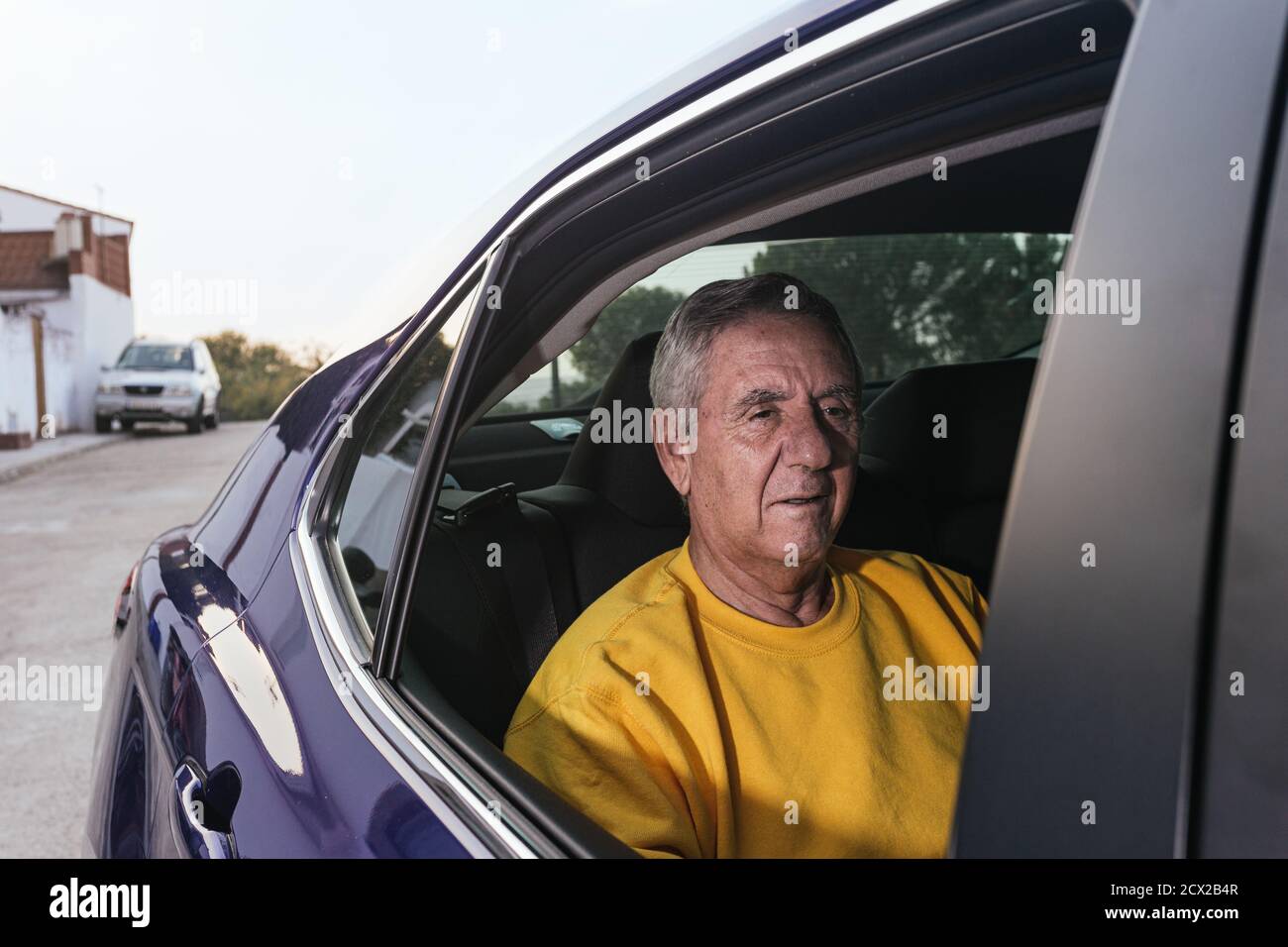 Ein alter Mann, der auf dem Rücksitz eines sitzt Elektroauto bei geöffnetem Fenster Stockfoto