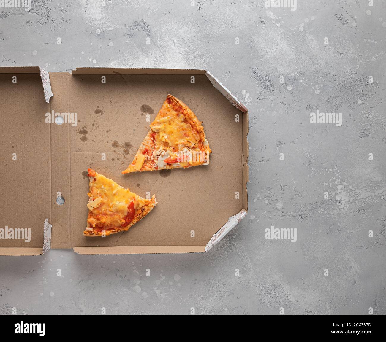 Teilweise sichtbare gebrauchte geöffnete Pizzabox mit zwei hässlichen Stücken kalte Pizza, Flecken und Krümel innen auf texturiertem grauen Hintergrund. Horizontale Ausrichtung. Stockfoto