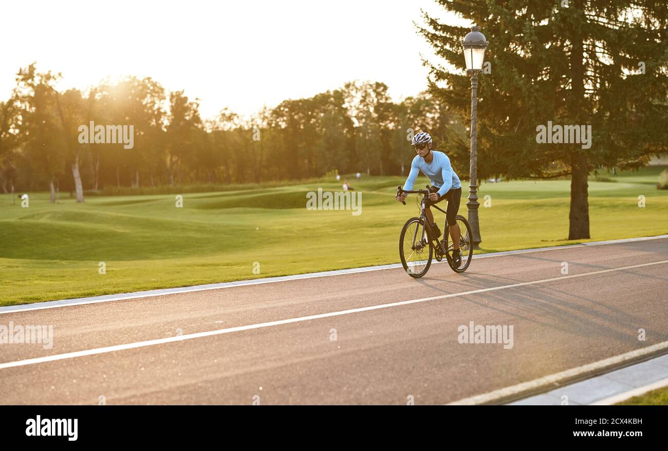 Athletic Mann in Sportbekleidung Radfahren im Stadtpark bei Sonnenuntergang, Fahrrad entlang einer Straße fahren. Gesunder aktiver Lebensstil und Sportkonzept Stockfoto