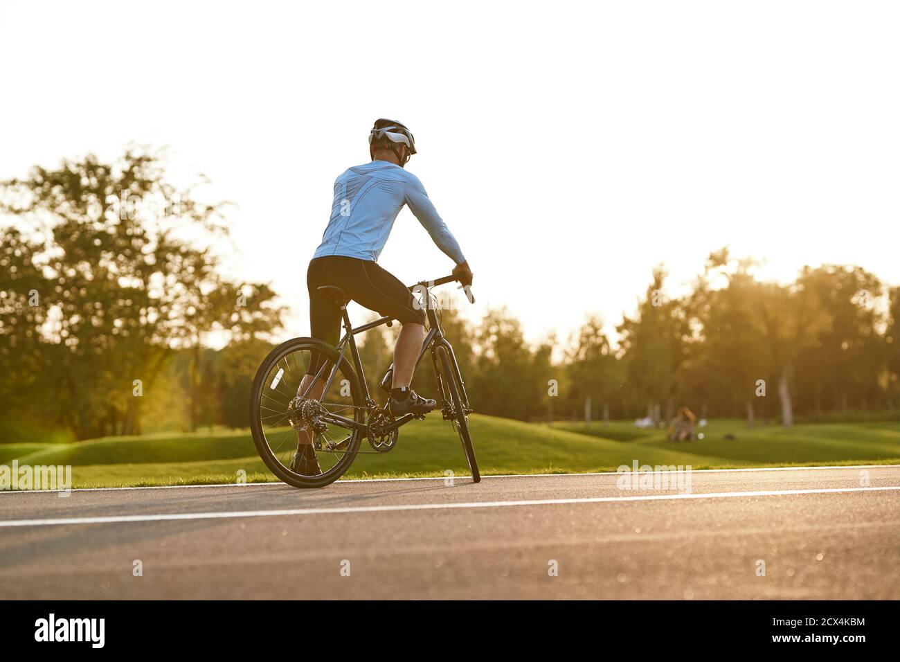 Bereit zum Fahren. Rückansicht des athletischen Mannes in der Sportbekleidung, der bei Sonnenuntergang im Freien radelt, professioneller Rennfahrer, der mit dem Fahrrad auf der Straße steht und einen atemberaubenden Blick auf die Natur genießt. Aktiver Lebensstil und Sport Stockfoto