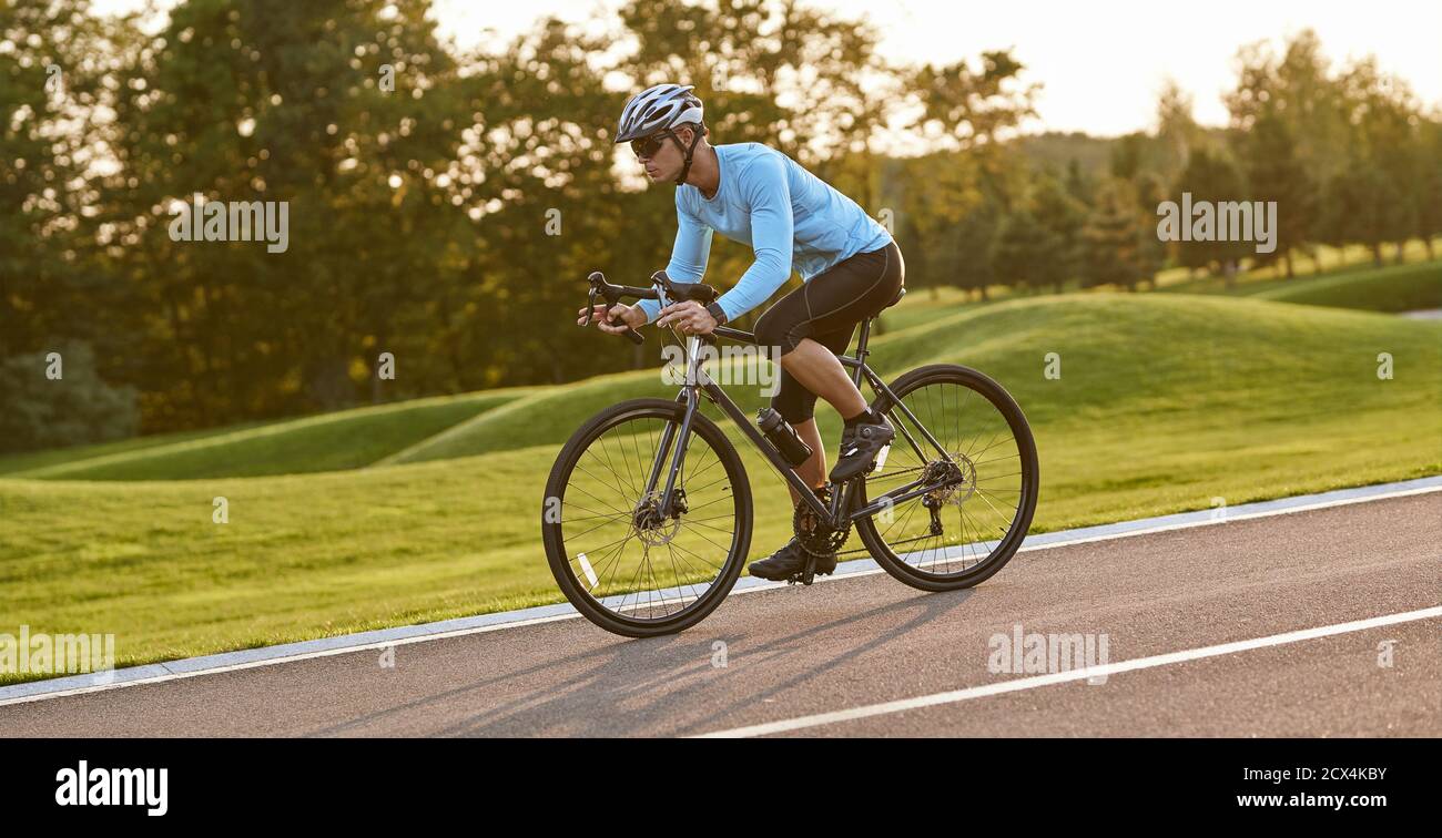 Professionelle Fahrrad-Racer in Aktion. Seitenansicht eines jungen Sportlers in Sportkleidung, der bei Sonnenuntergang Mountainbike fährt. Gesunder aktiver Lebensstil und Sportkonzept Stockfoto