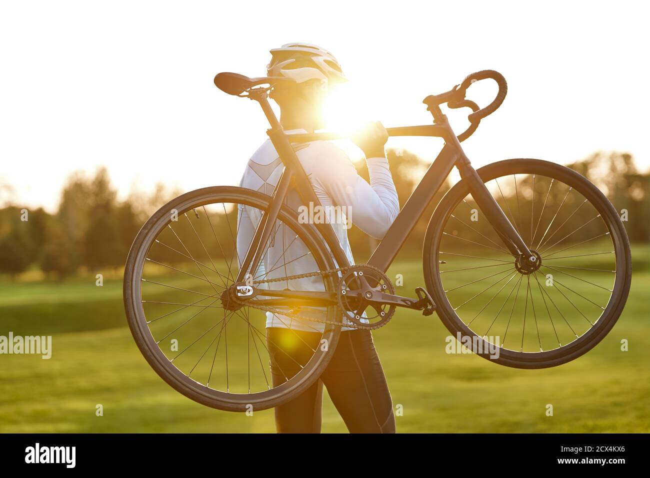 Starker Sportler in Sportbekleidung hält ein Fahrrad, während er im Park bei Sonnenuntergang steht, im Freien radelt und einen atemberaubenden Blick auf die Natur genießt. Aktiver Lebensstil und Sport Stockfoto