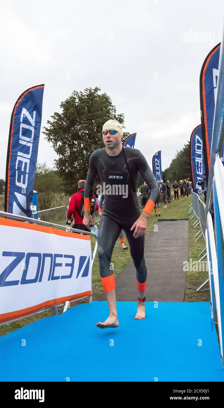 Elite männliche Profisportler, die sich in ihren Nassanzügen auf das erste Event, das Schwimmen, beim letzten Triathlon des Jahres vorbereiten. Stockfoto