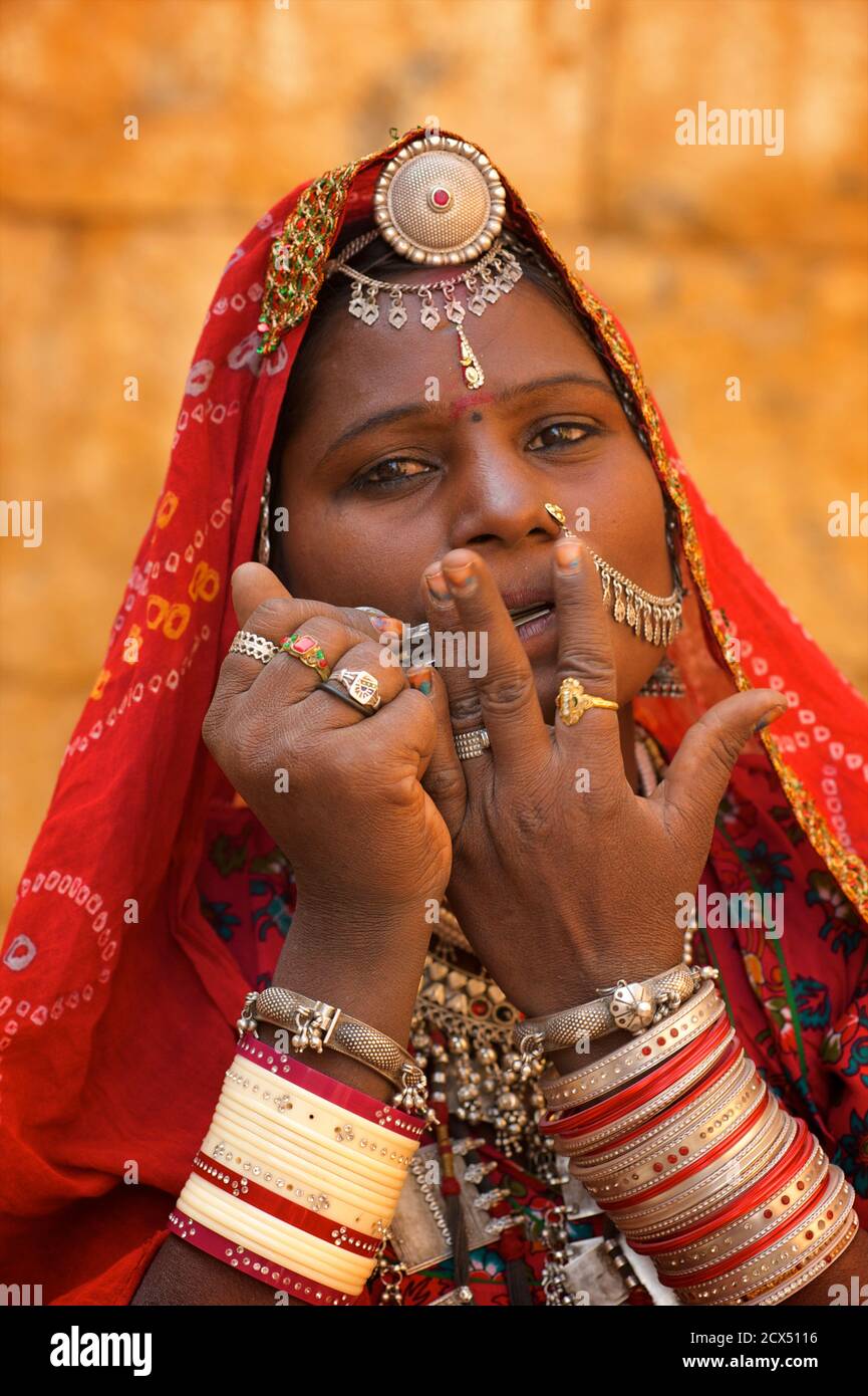 Portrait einer Rajasthani Frau in unverwechselbaren Rajasthani Kleid und Schmuck spielen eine Maultrommel, Jaisalmer, Indien. Dieses Bild enthält kulturell relevantes Material: 1. Rajasthani ethnischen Schmuck. 2. Ein Sari ist ein südasiatisches Frauenkleid, das aus einem Tuch mit einer Länge von 4 bis 8 Metern und einer Breite von 60 bis 1,20 Metern besteht, das normalerweise um die Taille gewickelt ist, wobei ein Ende über die Schulter drapiert ist und das Mittelriff entblößte. Der Sari wird normalerweise über einem Petticoat getragen. Der Sari ist mit Gnade verbunden und gilt weithin als Symbol der indischen Kultur. Stockfoto