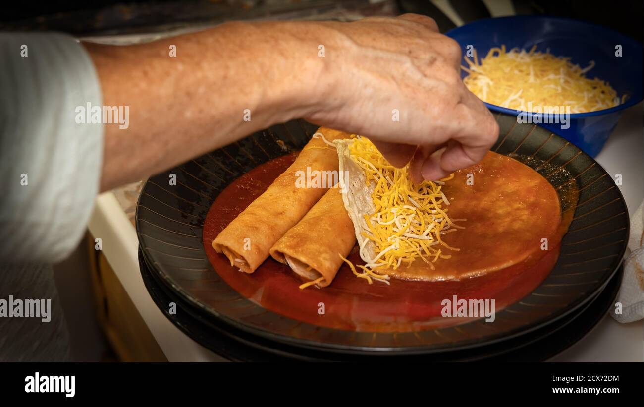 Ein Koch fügt zerkleinerten Käse zu hausgemachten Entomatadas, die in der Küche zubereitet werden. Stockfoto