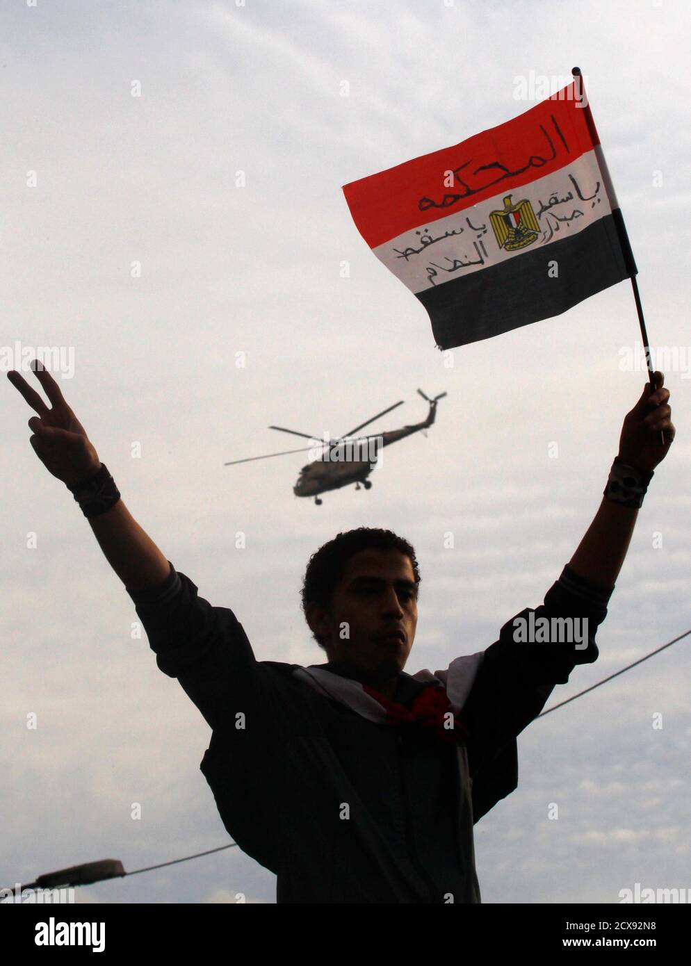 Ein Demonstrant hält eine ägyptische Flagge als eine Armee Hubschrauber fliegen Overhead Tausende von Anti-Regierungs-Demonstranten versammelten sich für einen sechsten Tag am Tahrir-Platz in Kairo 30. Januar 2011. Ägyptische Luftwaffe Kampfflugzeuge summte tief über Cairo am Sonntag, den Helikopter schwebte über und zusätzliche Truppe LKW erschien an einem zentralen Platz, wo Demonstranten ein Ende der Herrschaft von Präsident Hosni Mubarak forderten.  REUTERS/Yannis Behrakis (Ägypten - Tags: Politik Unruhen Militär) Stockfoto