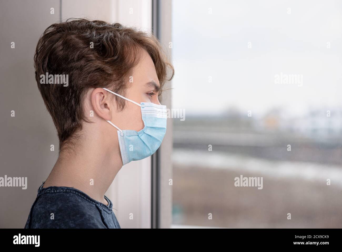 Coronavirus-Quarantäne. Kind trägt Schutzmaske während Grippe-Virus, Blick aus dem Fenster. Selbstisolierung. Teen junge gezwungen zu bleiben zu Hause. Stockfoto