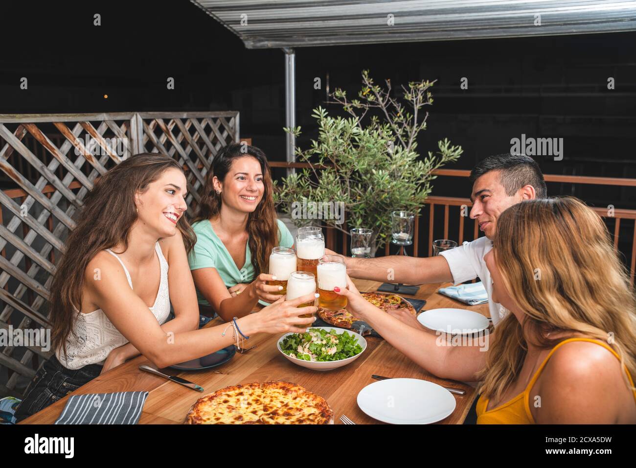 Freunde jubeln mit Biergläsern an einem Tisch - Gruppe von multirassischen Menschen toasten und klirren Getränke an jedem Andere Stockfoto