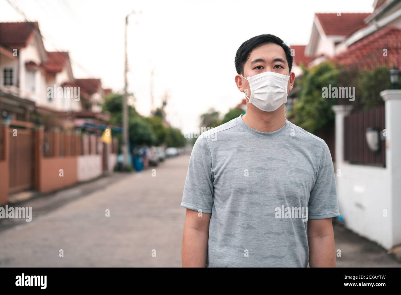 Junger asiatischer Mann trägt eine Gesichtsschutzmaske vor seinem Haus im Freien. Tragen einer Gesichtsmaske vor dem Verlassen des Hauses. Stockfoto