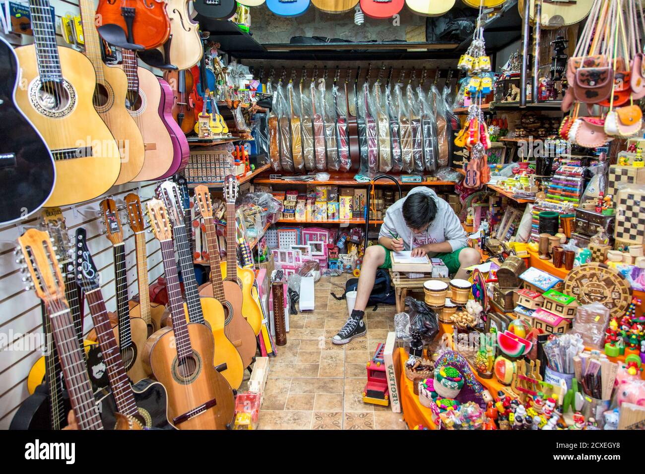 Ein junger Mann hunched über Schreiben in einem Marktstand Mit Gitarren in Mexiko-Stadt Stockfoto