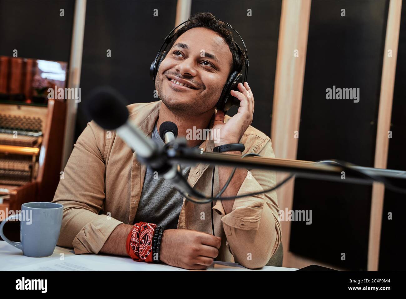 Glücklicher junger männlicher Radiomoderator, der beim Rundfunk im Studio mit Mikrofon und Kopfhörern zur Seite schaut Stockfoto