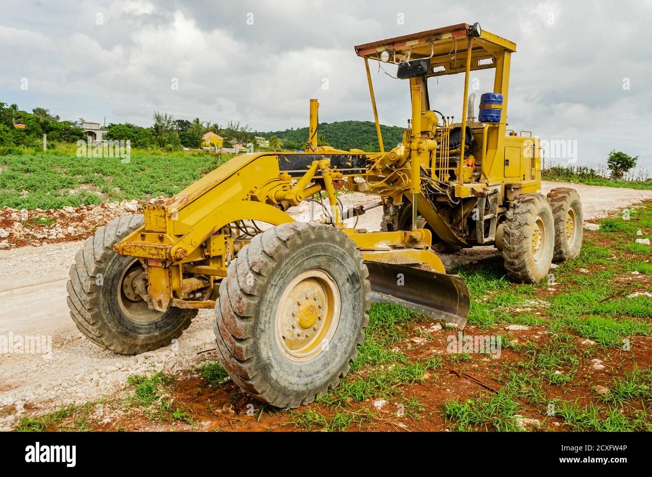 Ein Motorgrader parkt am Rande einer Straße, die im Bau ist, mit drei Rädern auf der mergurten überdachten Fahrbahn und den anderen drei auf der Stockfoto