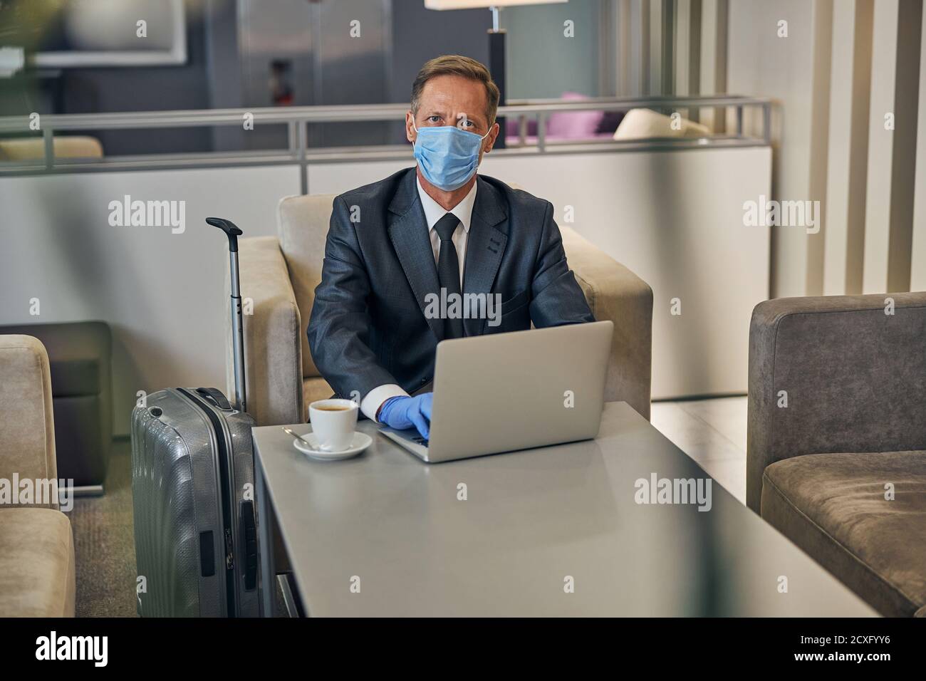 Reifer Geschäftsmann mit Laptop in der Flughafenlounge während der Quarantäne Stockfoto