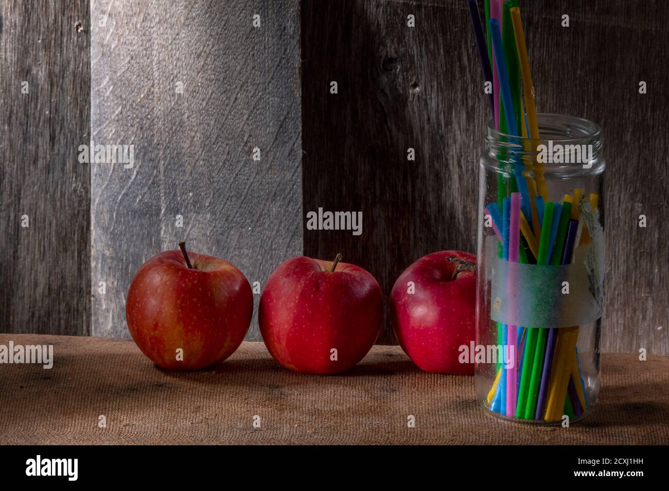 Nahaufnahme Foto von drei natürlichen roten Äpfeln und Plastikstrohhalmen In Glas Glas auf Holzhintergrund Stockfoto