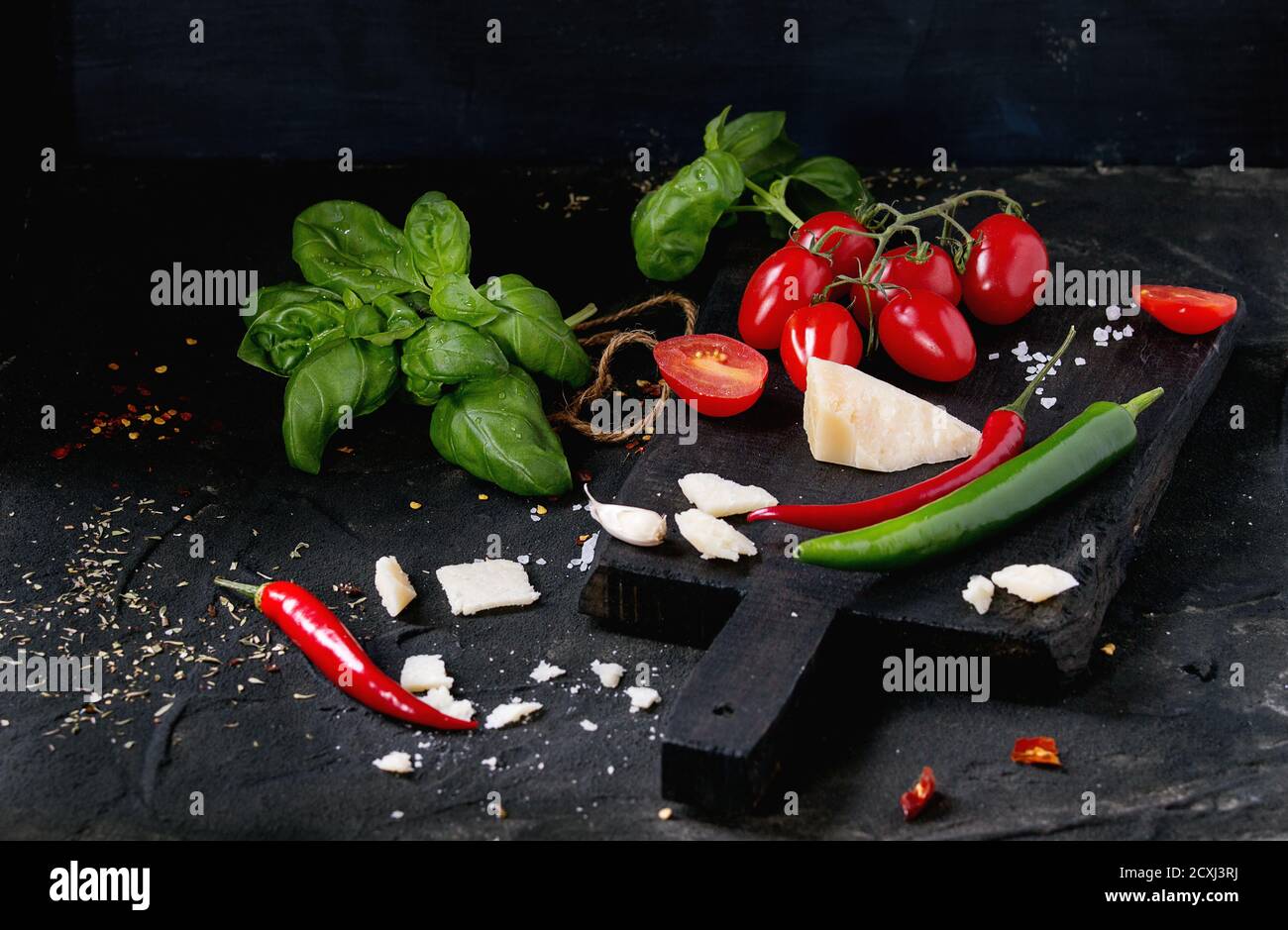 Zutaten für Pasta Sauce Tomaten, Basilikum, Knoblauch, Chili und Parmesan Käse auf Holz Schneidebrett auf schwarzem texturierten Hintergrund Stockfoto