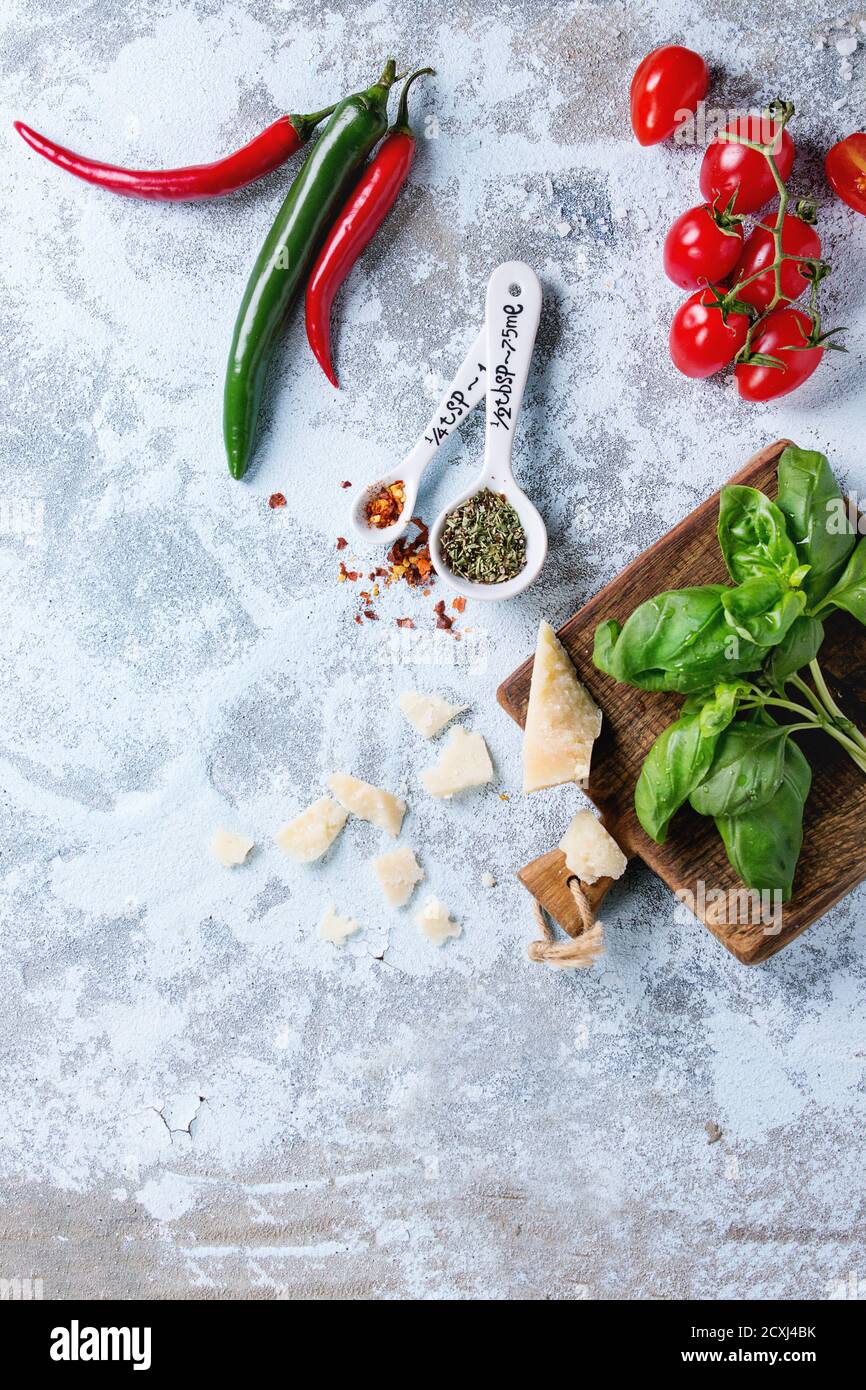 Zutaten für Pasta-Sauce Tomaten, Basilikum, Chilischoten und Parmasan-Käse auf Holzschneidebrett auf weißem Strukturhintergrund. Flach liegend Stockfoto