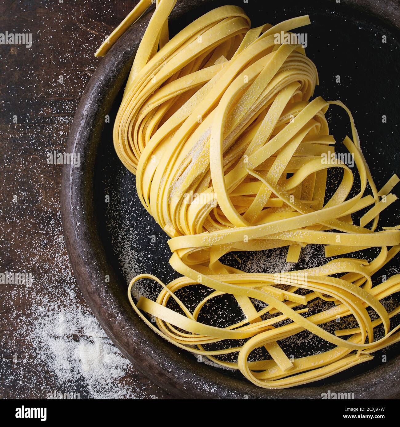 Rohe hausgemachte italienische Pasta-Tagliatelle mit Mehl in alten Tontäfelchen auf dunklem Holzhintergrund. Draufsicht mit Platz für Text. Quadratisches Bild Stockfoto