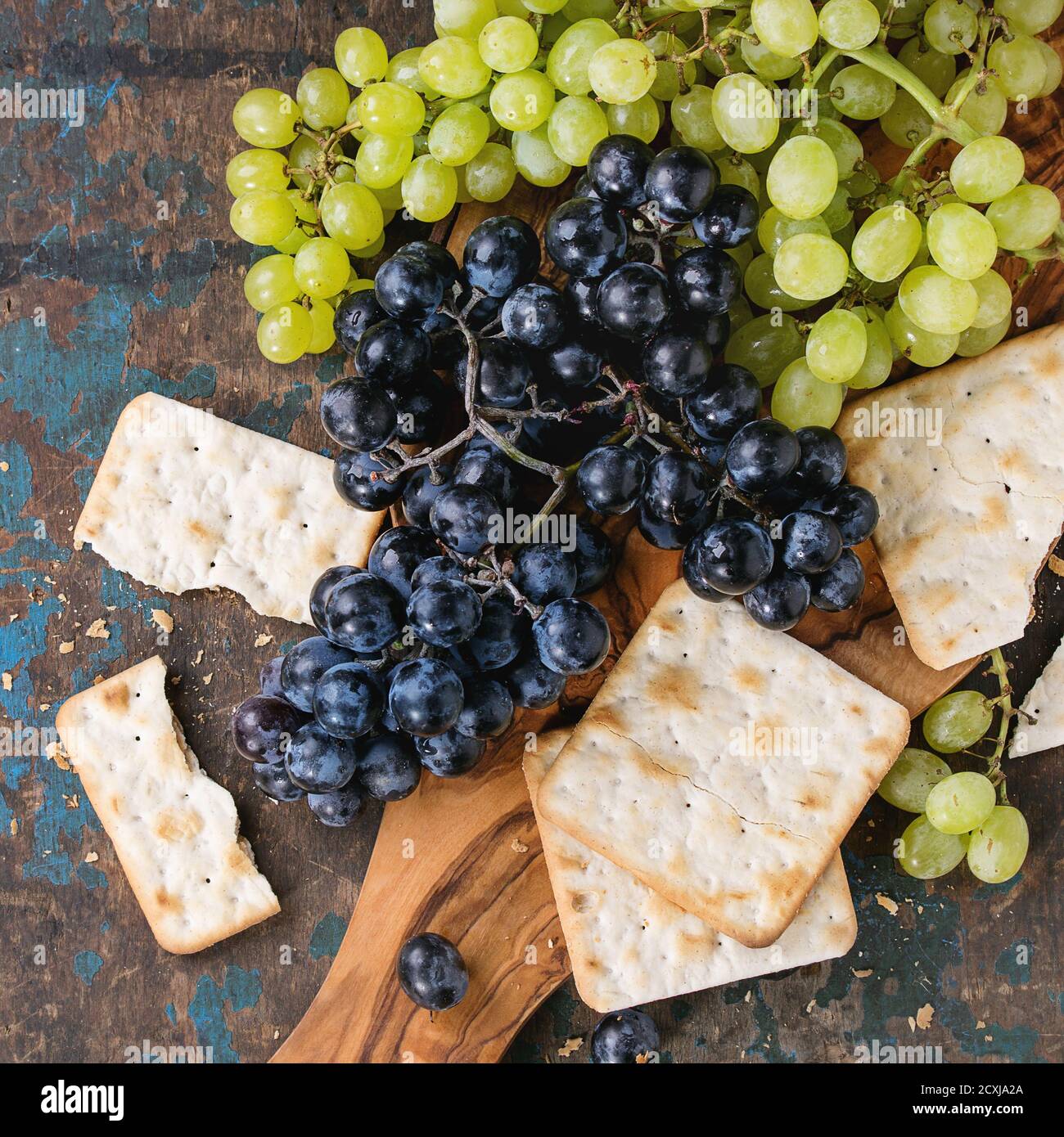 Trauben von reifen feuchten roten und weißen Trauben mit Crackern Snack auf Olivenholz Schneidebrett über alten dunklen Holzhintergrund. Draufsicht. Quadratisches Bild Stockfoto