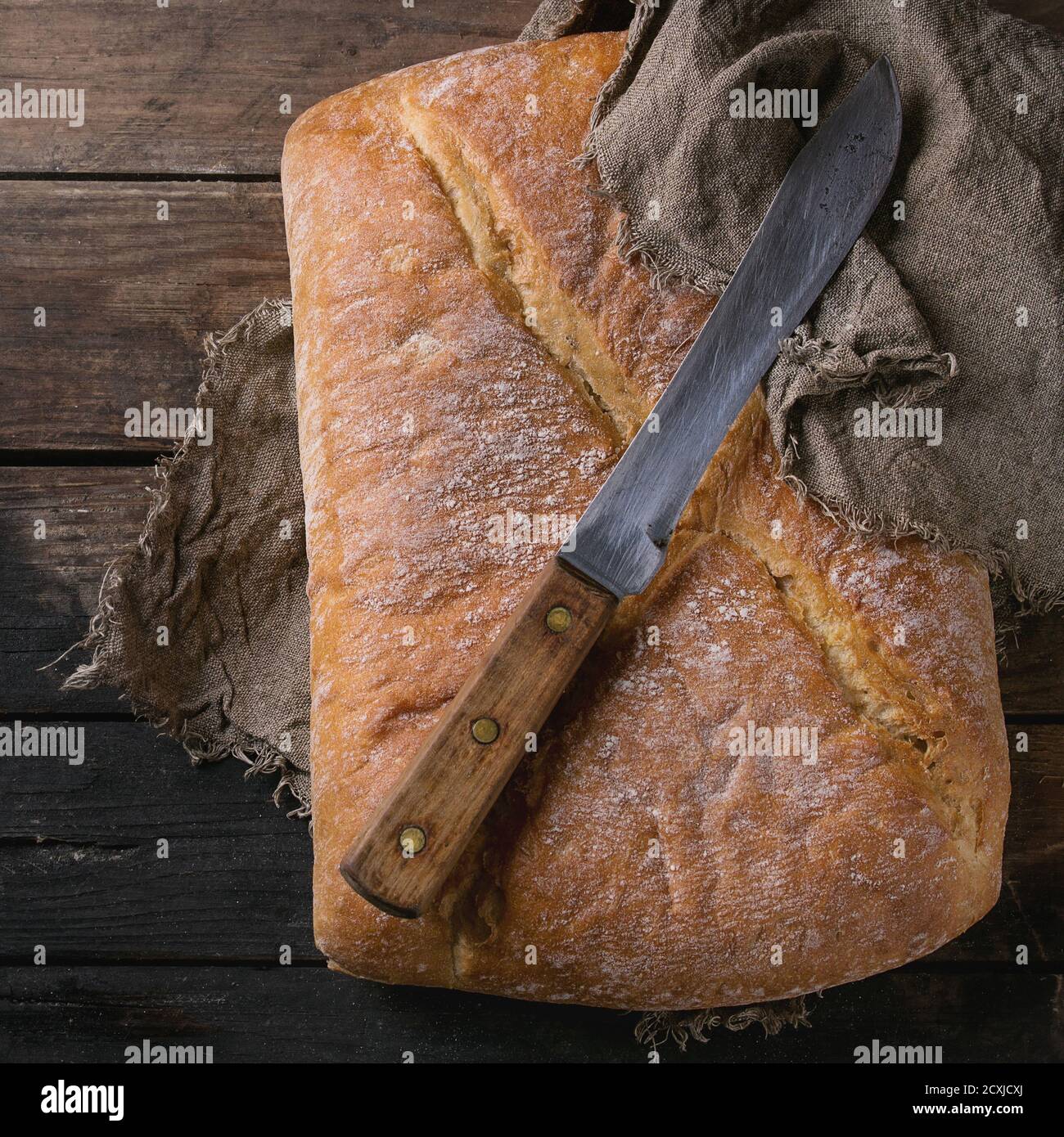 Ganze frisch gebackene handwerkliche Brot unter Sacktuch mit Vintage-Messer über alten Holzhintergrund. Overhead-Ansicht. Speicherplatz kopieren. Quadratisches Bild Stockfoto
