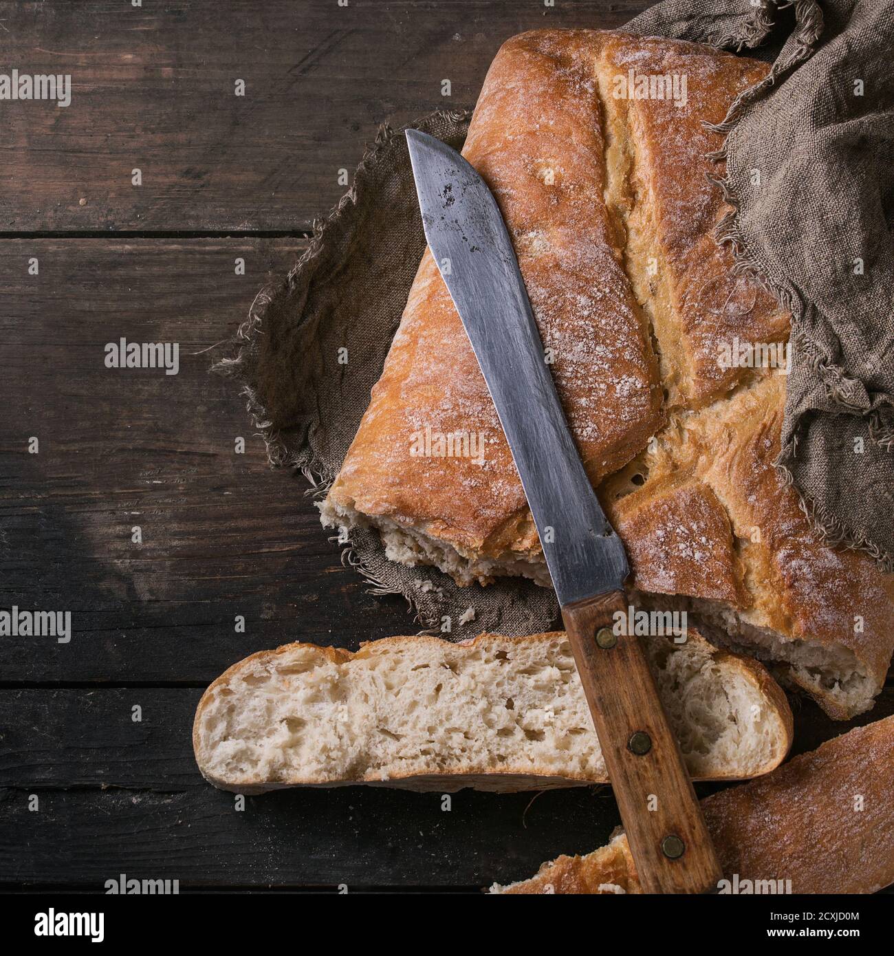 Frisches handwerkliches Brot in Scheiben unter Sacktuch mit Vintage-Messer auf altem Holzhintergrund. Overhead-Ansicht mit Kopierbereich. Quadratisches Bild Stockfoto