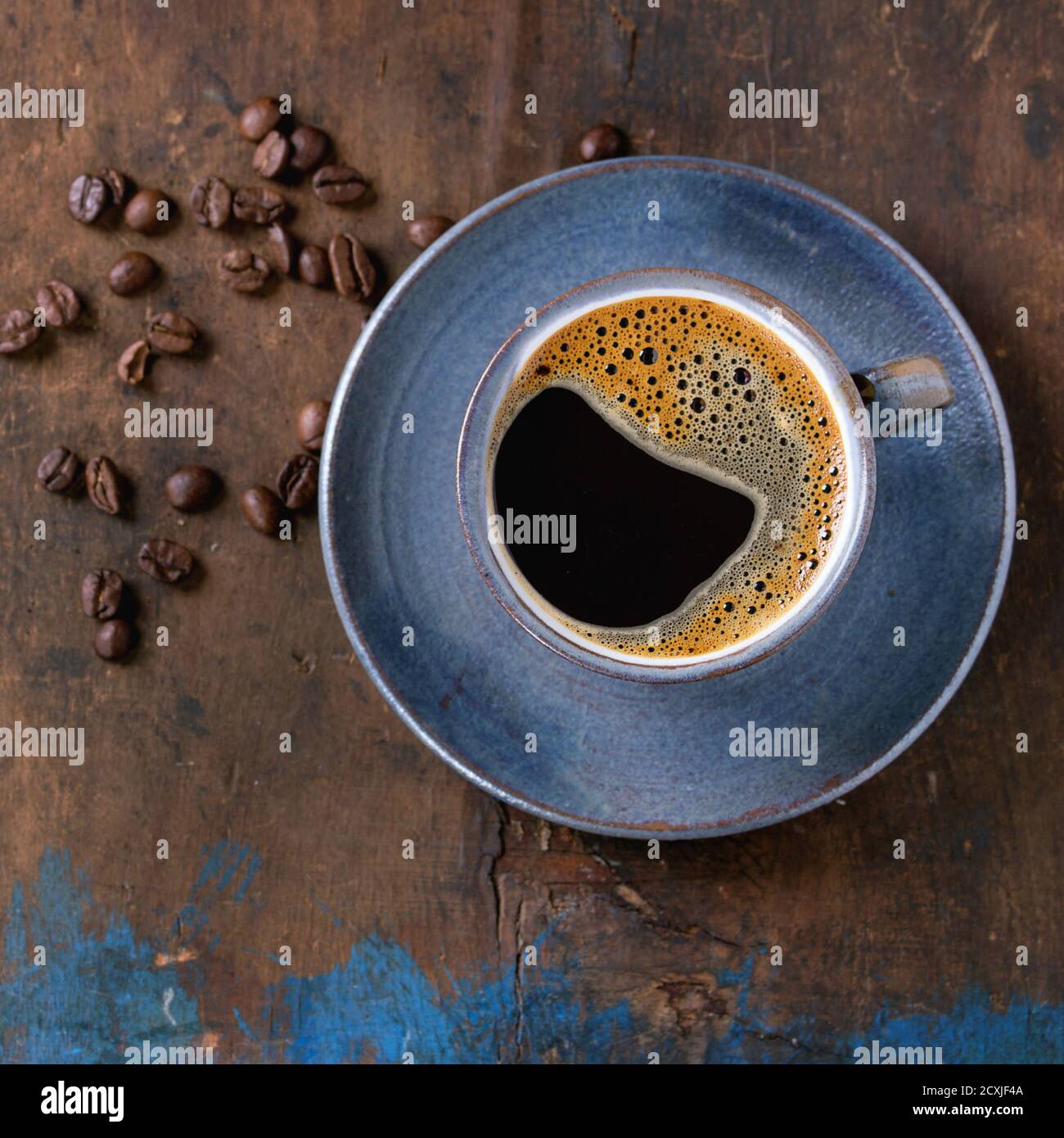 Blaue Keramik Tasse schwarzen heißen Kaffee auf Untertasse, serviert mit Kaffeebohnen über alten Holz strukturierten Hintergrund. Draufsicht. Speicherplatz kopieren. Quadratisches Bild Stockfoto