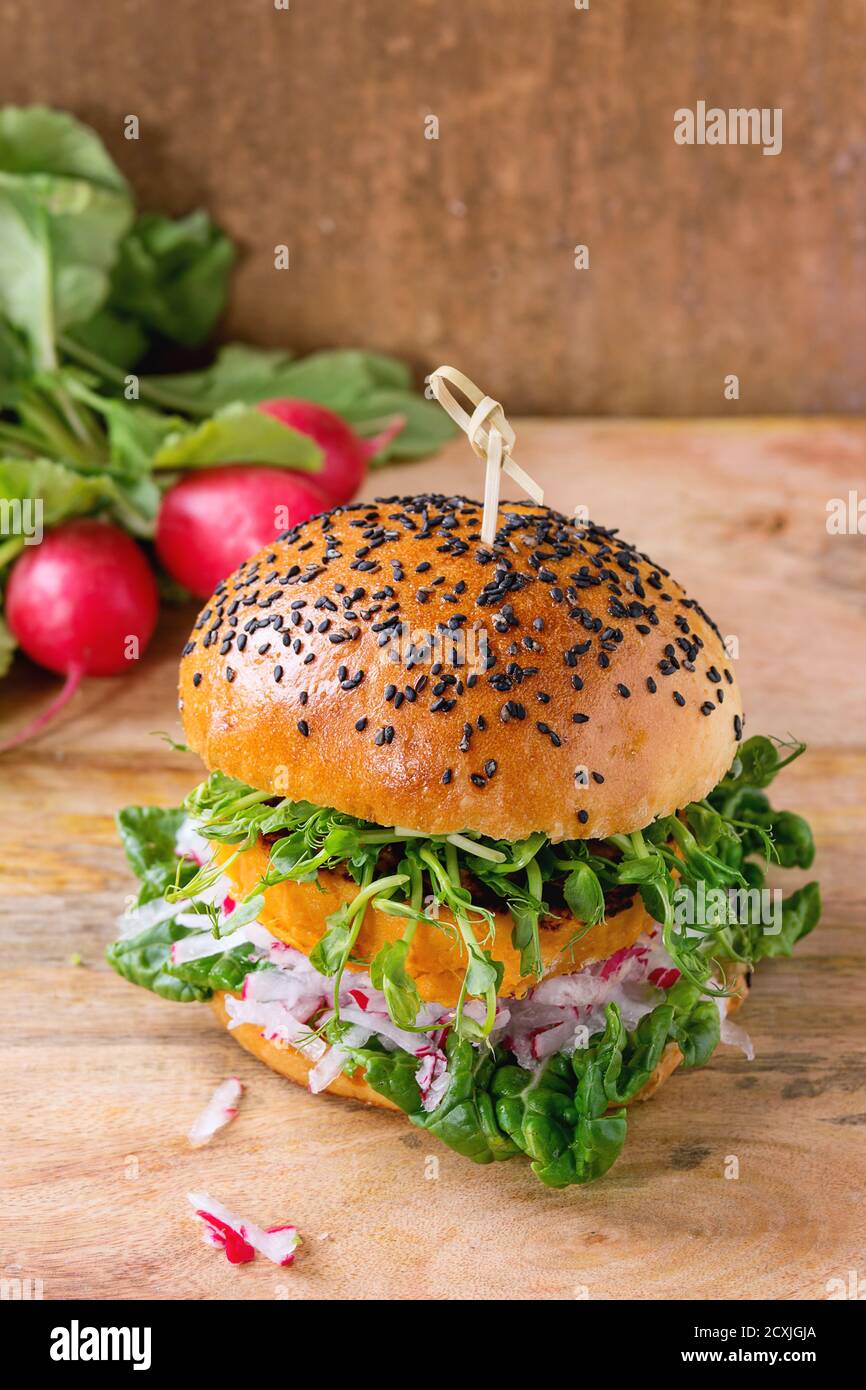 Hausgemachter Gemüse-Süßkartoffel-Burger mit frischem Rettich und Erbsensprossen serviert mit einem Bündel Rettich auf Holz strukturierten Hintergrund. Stockfoto