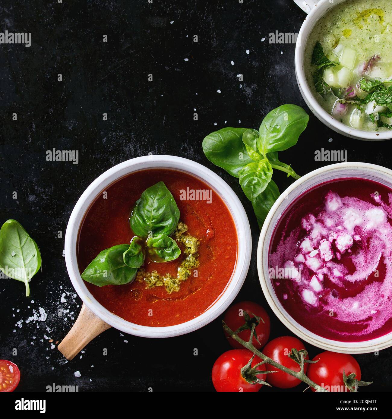 Auswahl an kalten vegetarischen Suppen Gazpacho Gurke mit Minze, Rote Beete mit Feta-Käse, Tomaten mit grünem Pesto, serviert mit Gewürzen in Tassen über b Stockfoto
