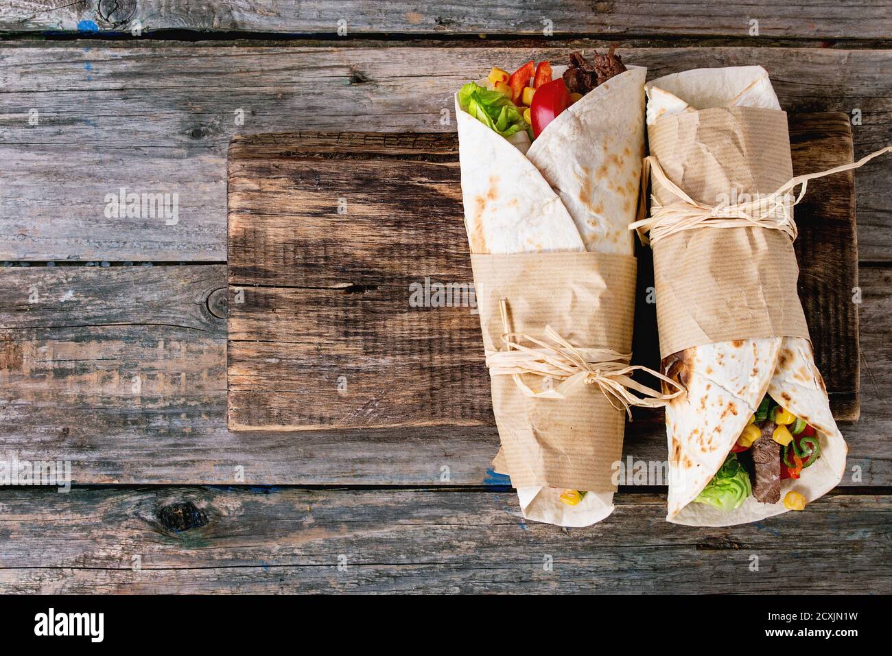 Mexikanisches Abendessen. Zwei tapeierte Tortillas Burrito mit Rindfleisch und Gemüse auf altem Holzhintergrund. Flach liegend. Mit Kopierbereich Stockfoto