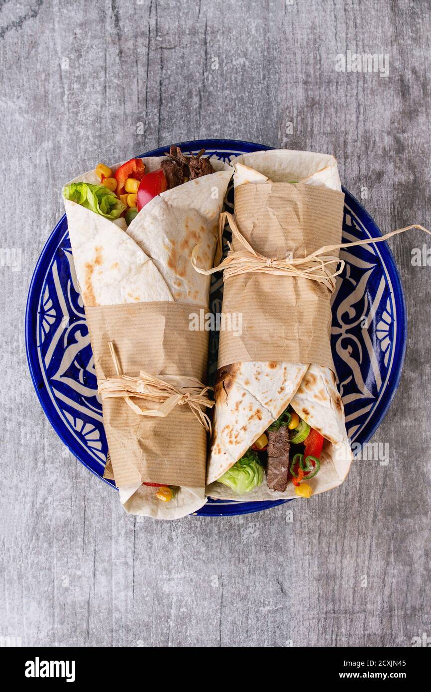 Mexikanisches Abendessen. Zwei tapeierte Tortillas Burrito mit Rind und Gemüse serviert auf blau dekorativen Keramikplatte auf weißem Holzhintergrund. Fla Stockfoto