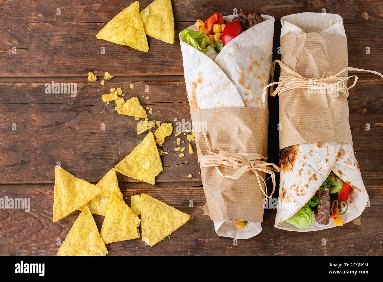 Mexikanischer Stil. Abendessen. Zwei tapeierte Tortillas Burrito mit Rindfleisch und Gemüse serviert mit Nachos Chips Sauce über alten Holzhintergrund. Flach liegend Stockfoto