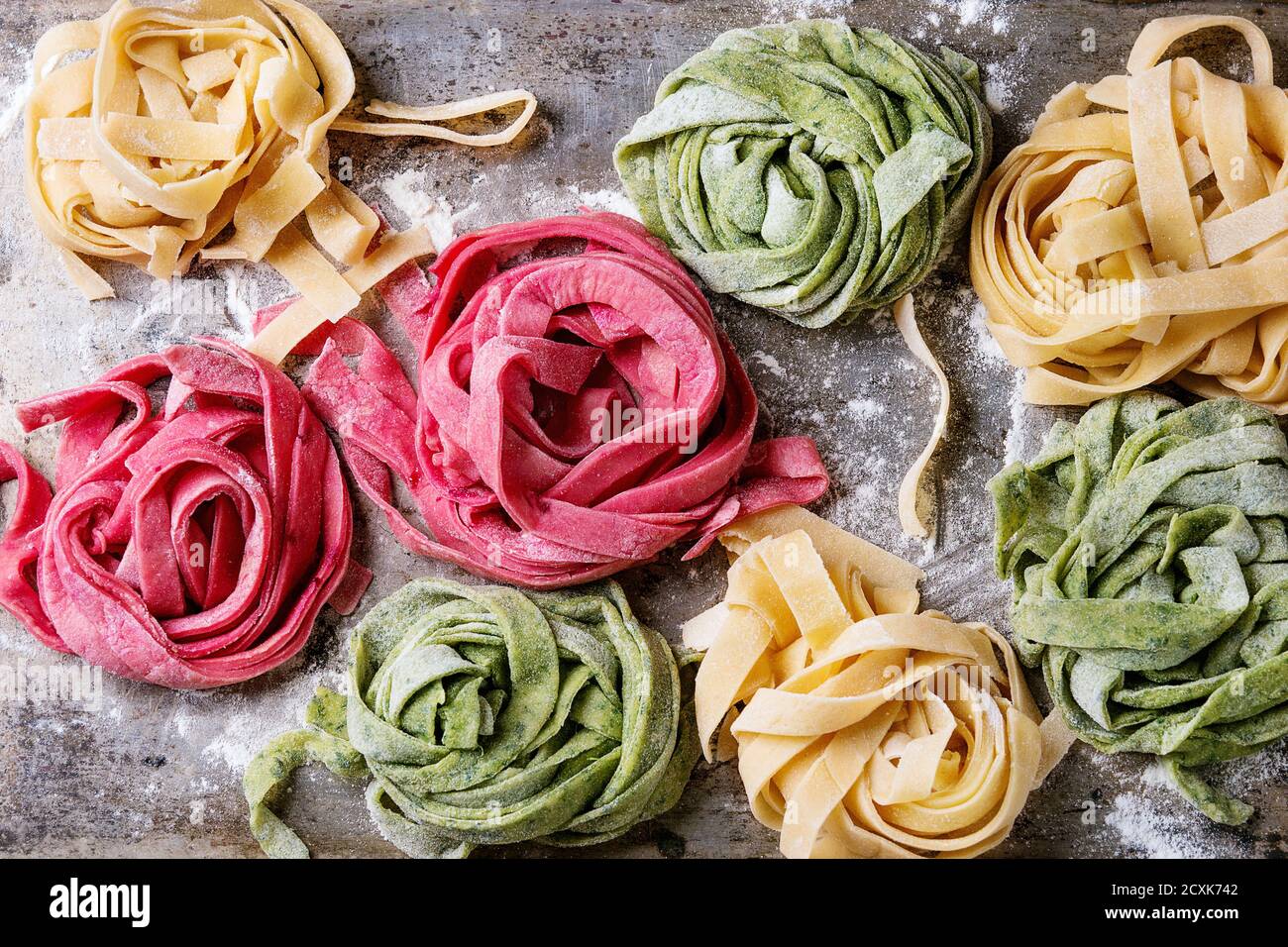 Vielzahl von farbigen frischen rohen hausgemachte Teigwaren Tagliatelle grün Spinat, rosa rote Beete und gelb mit Mehl über alte Metall Textur Hintergrund. Stockfoto