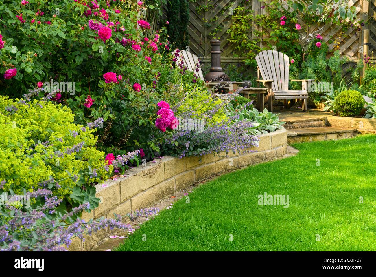 Landschaftlich schöner, sonniger privater Garten (modernes Design, farbenfrohe Sommerblumen, Randpflanzen, Sitzmöbel auf der Terrasse, Rasen) - Yorkshire, England, Großbritannien Stockfoto