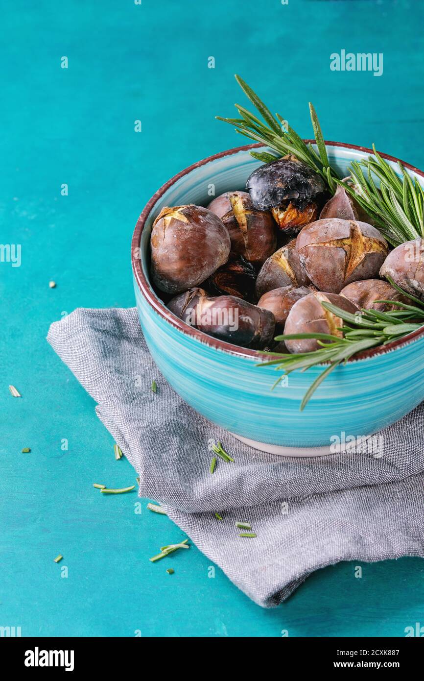 Gebratene Kastanien in der Asche mit Rosmarin in Türkis Keramikschale auf Textile Serviette über hellen blauen hölzernen Hintergrund. Stockfoto
