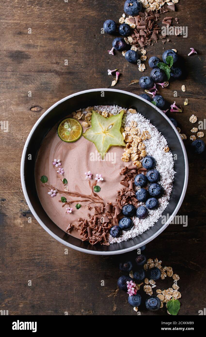 Smoothie Schüssel gesundes Frühstück. Schokolade Joghurt mit Heidelbeeren, Müsli, Kokos, Limette und Karambole über dunkle Holz Textur Hintergrund. Zeichnung Stockfoto