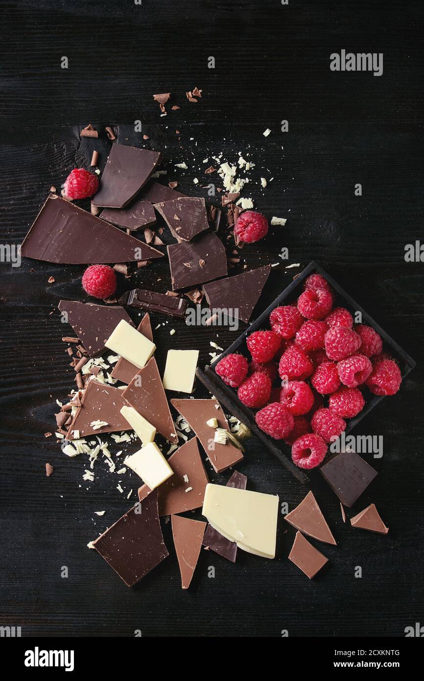 Vielzahl von dunklen, verbrannt Milch und weiße Schokolade mit frischen Himbeeren in schwarzer Holzbox über schwarz hacken Holz Hintergrund. Ansicht von oben mit dem Raum. C Stockfoto