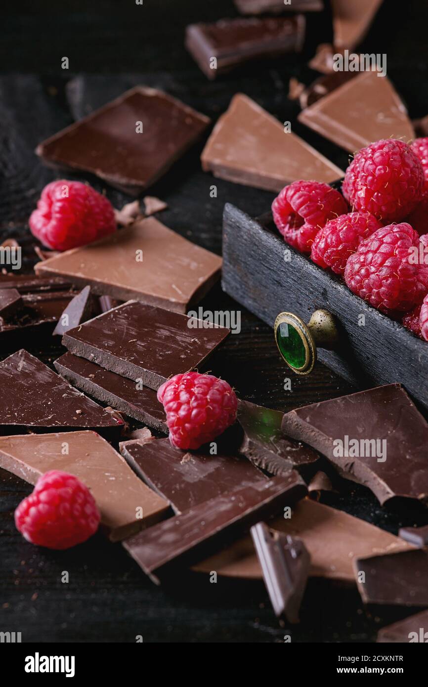 Dunkle und Milch Schokolade und Chips Späne hacken Schokolade mit frischen Himbeeren in schwarzer Holzbox über schwarzem verbranntem Holz hacken. CL Stockfoto